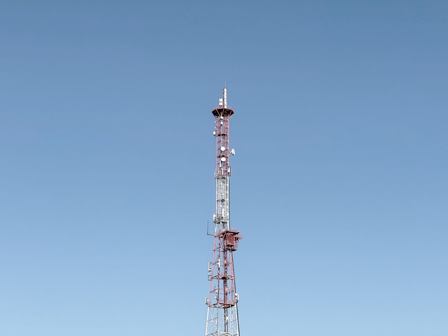 A tall communication tower set against a cloudless blue sky, symbolizing modern telecommunications.