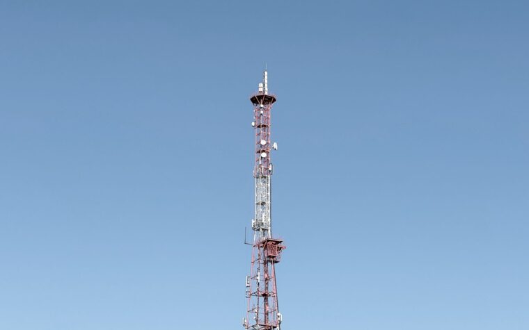 A tall communication tower set against a cloudless blue sky, symbolizing modern telecommunications.